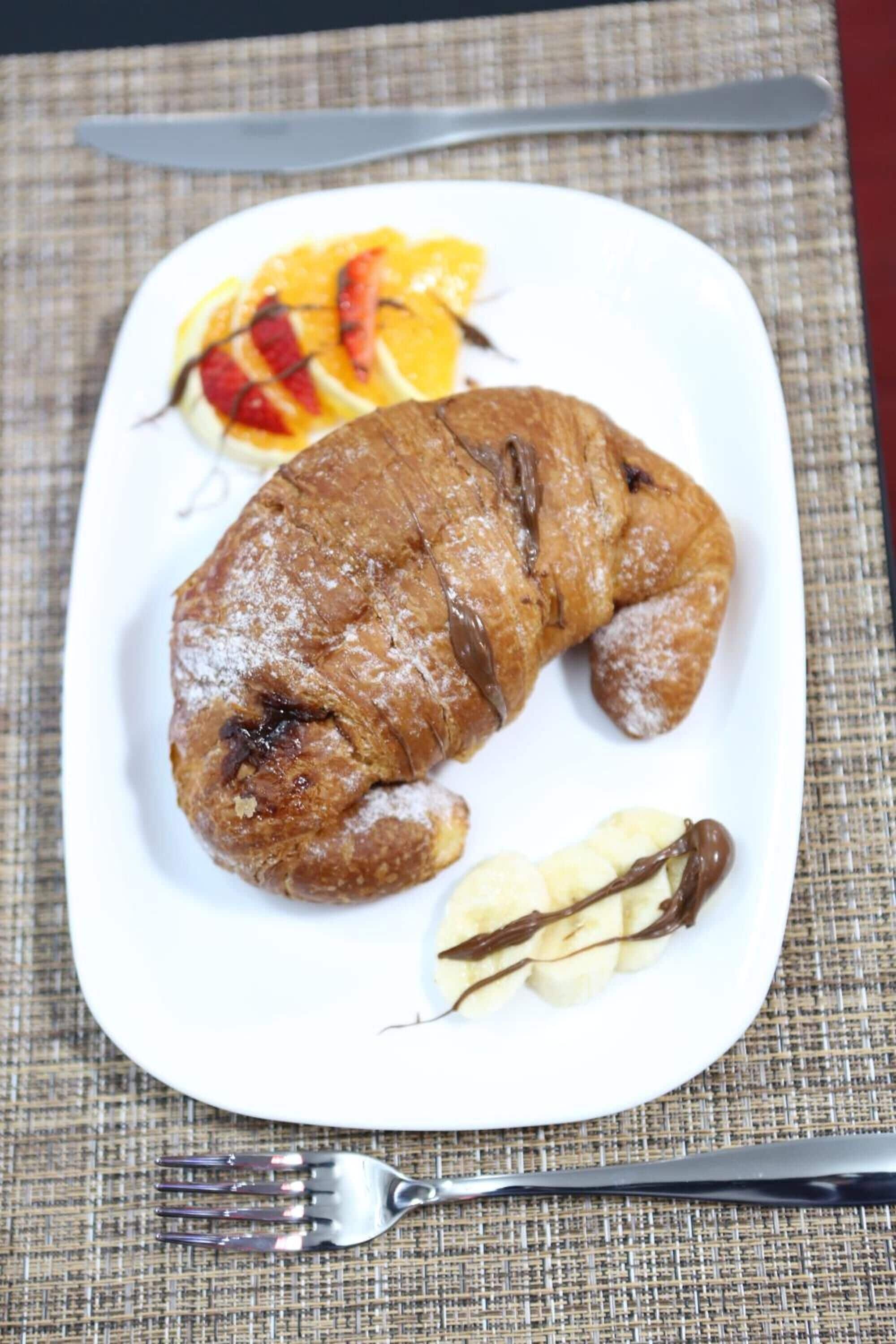 Un plato con un croissant, fruta cortada y un trozo pequeño de chocolate.
