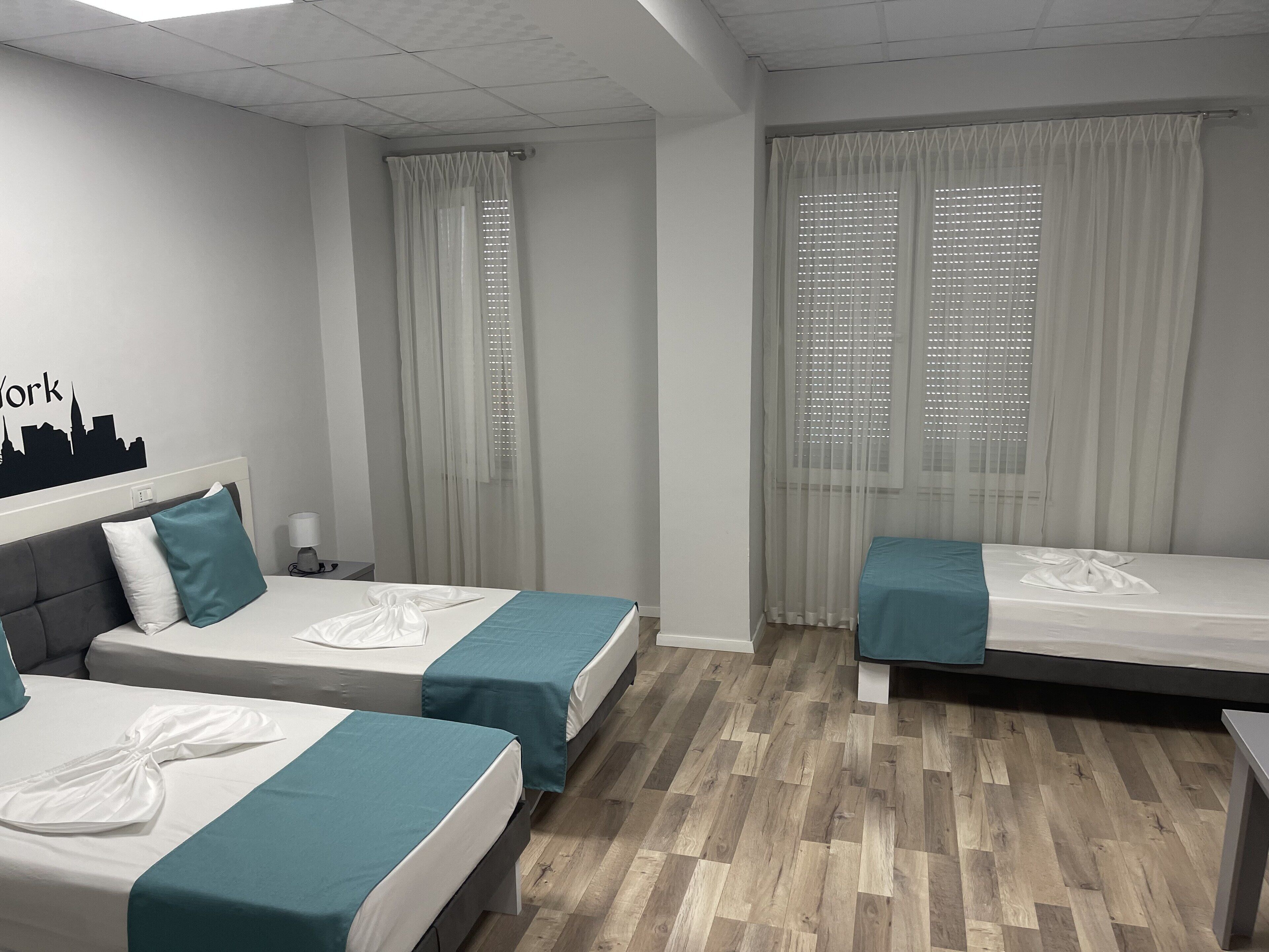 Habitación de hotel con dos camas individuales, una mesita de noche, una lámpara y una pared decorada con un diseño de paisaje urbano.