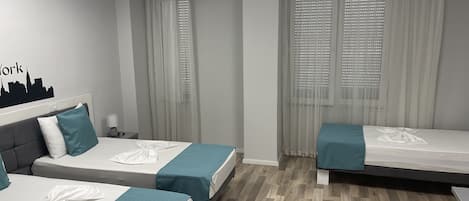 Habitación de hotel con dos camas individuales, una mesita de noche, una lámpara y una pared decorada con un diseño de paisaje urbano.