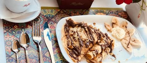 A breakfast setting with a plate of crepes, bananas, and a cup of coffee.