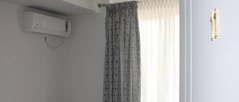 Una cama bien hecha con toallas, una lámpara de noche y una ventana con cortinas translúcidas.