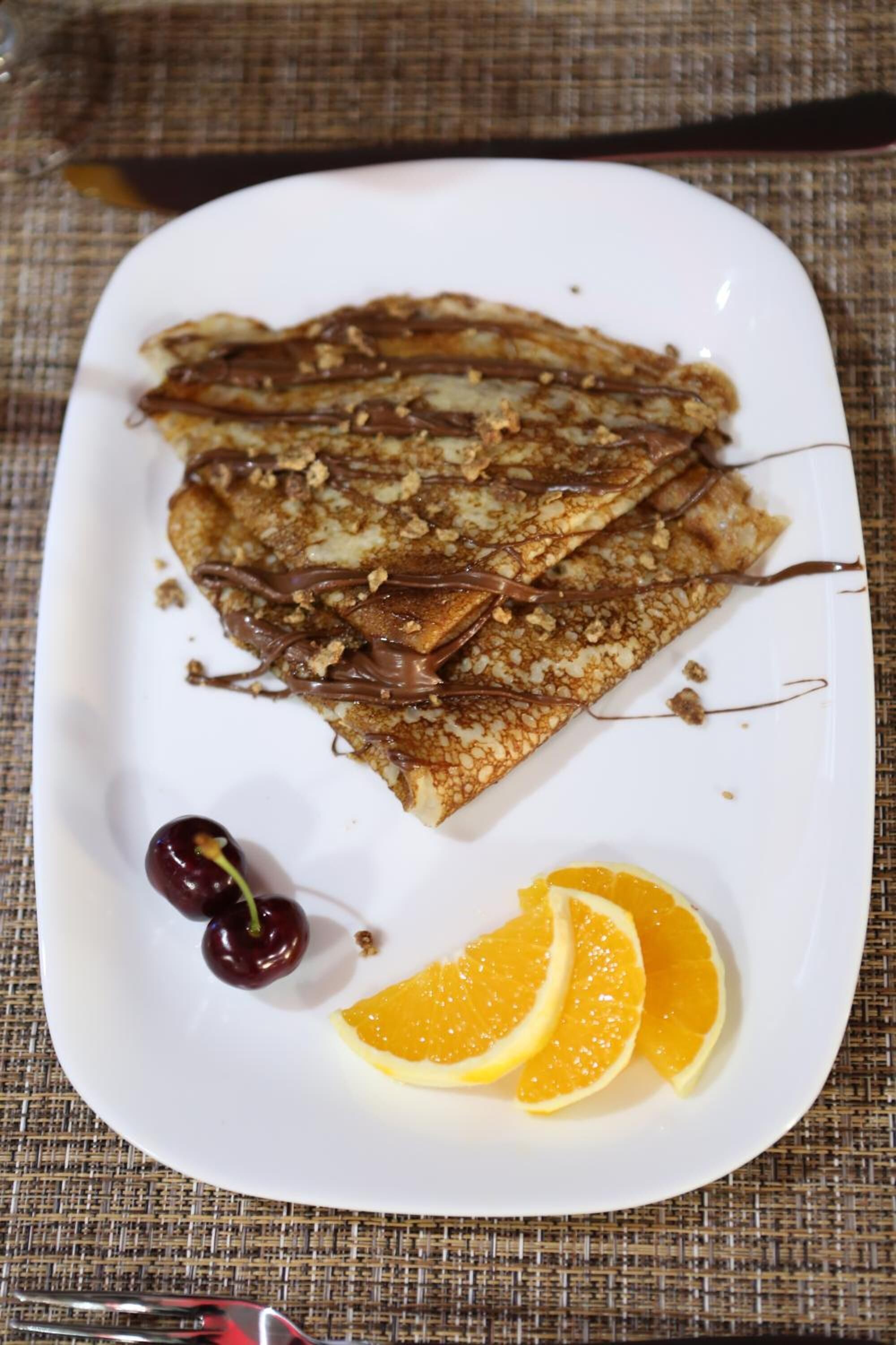 A plate of crepes with chocolate sauce and garnished with cherries and orange slices.