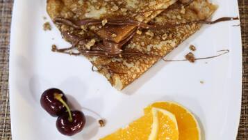 Une assiette de crêpes nappées de sauce au chocolat et garnie de cerises et de tranches d’orange.