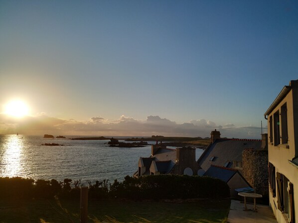 A coastal view with buildings, a clear sky, and the sun setting over the water. - Atypical fisherman's house, breathtaking sea view of the Iroise Sea (Porspoder)