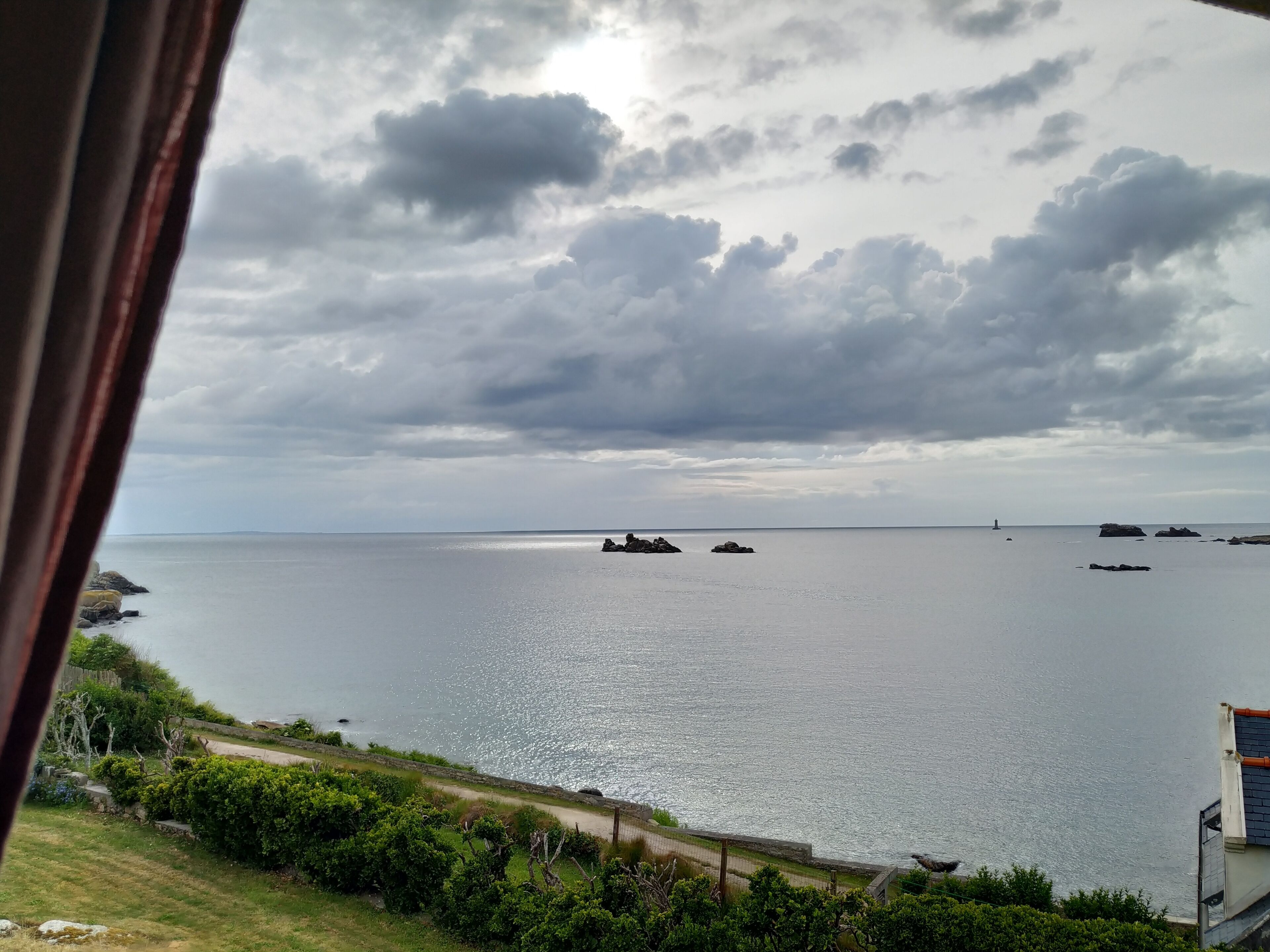 Une vue sur la côte, avec une mer calme, des affleurements rocheux et un phare au loin.