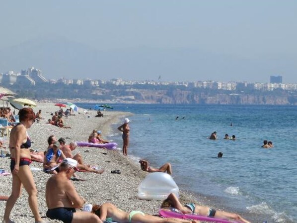 A crowded beach with people sunbathing and swimming.
