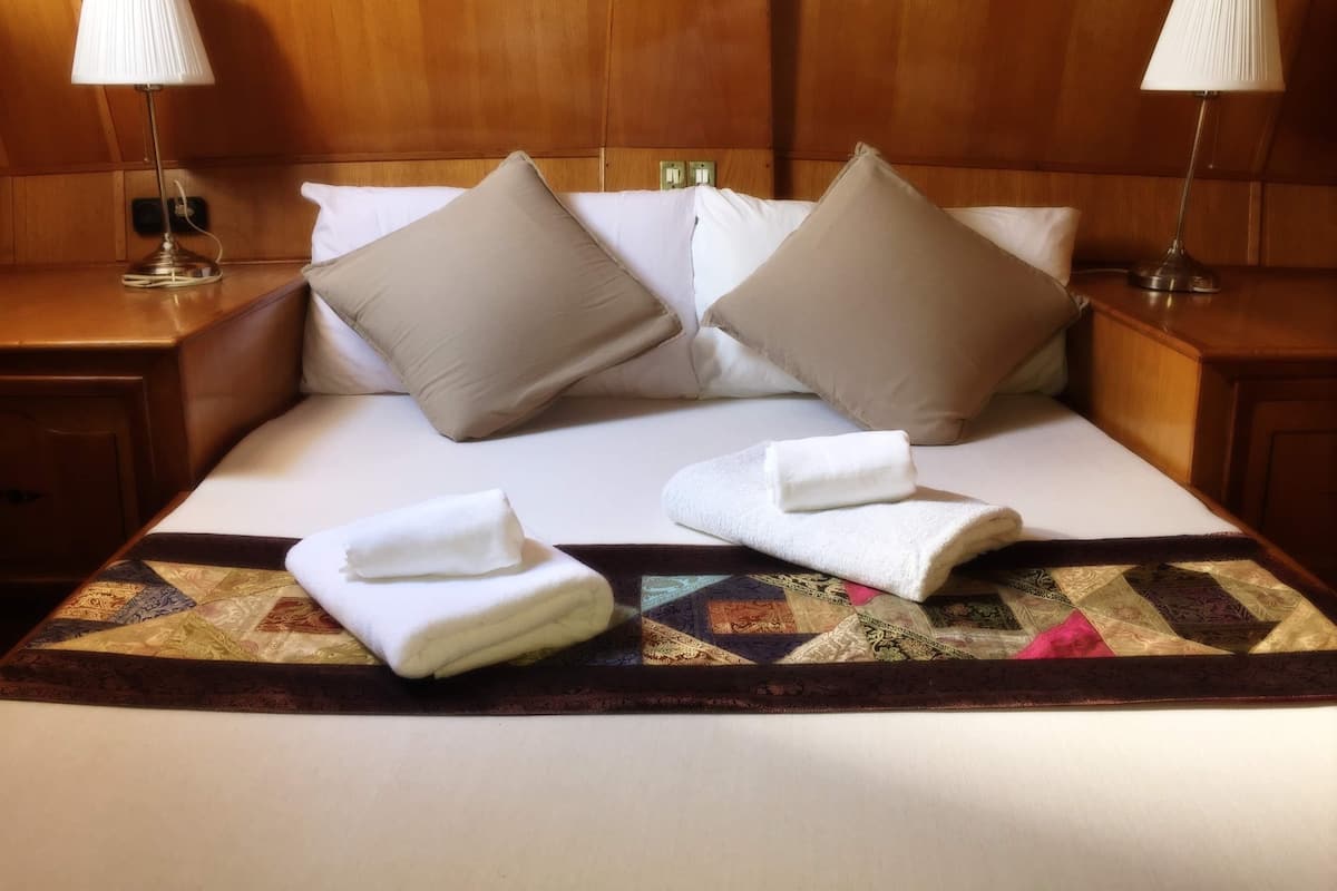 A neatly made bed with two pillows, a quilt, and two folded towels.