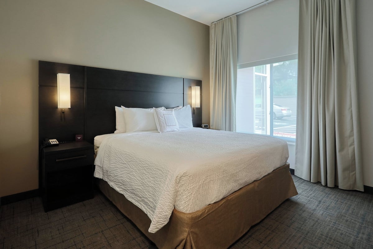 A hotel room with a large bed, a nightstand with a phone, and a window with curtains.