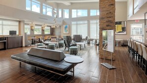 Eine geräumige Lobby mit modernem Design, ausgestattet mit einer großzügigen Sitzecke, einer Wand aus Naturstein und großen Fenstern für viel Tageslicht.