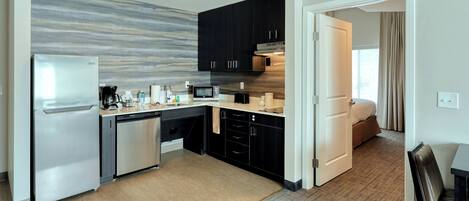 A modern kitchen with a refrigerator, microwave, and coffee maker. There is a small dining area with a table and chairs.