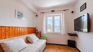 Une chambre confortable avec une tête de lit en bois, une grande fenêtre avec des rideaux, un téléviseur à écran plat et un haut-parleur.