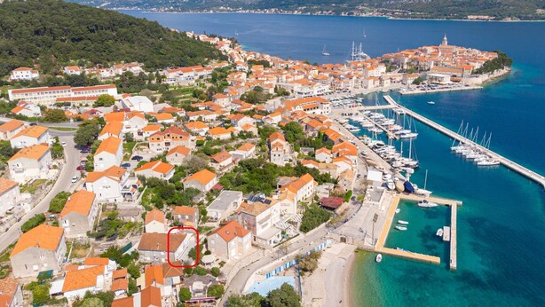 Vue aérienne d’une ville côtière avec un port de plaisance, des maisons aux toits orange et une mer d’un bleu limpide.