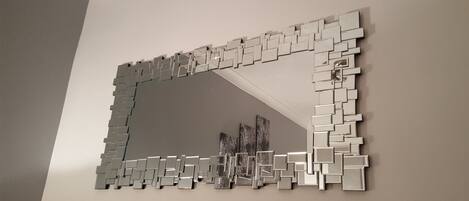A mirror with a geometric frame mounted on a plain wall.