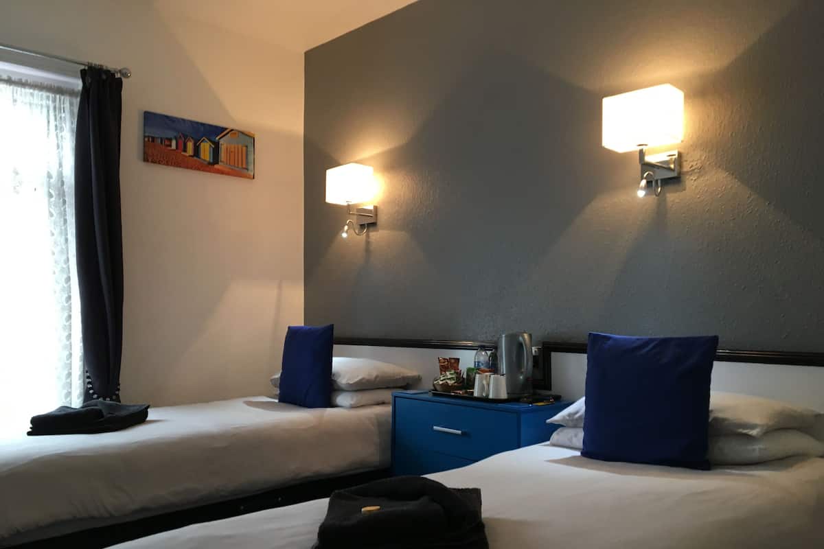 Una habitación de hotel con dos camas, una mesita de noche, una lámpara y un cuadro en la pared.