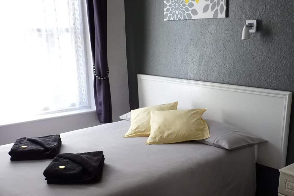 Habitación de hotel con cama, dos almohadas, una mesita de noche y ventana con cortinas.
