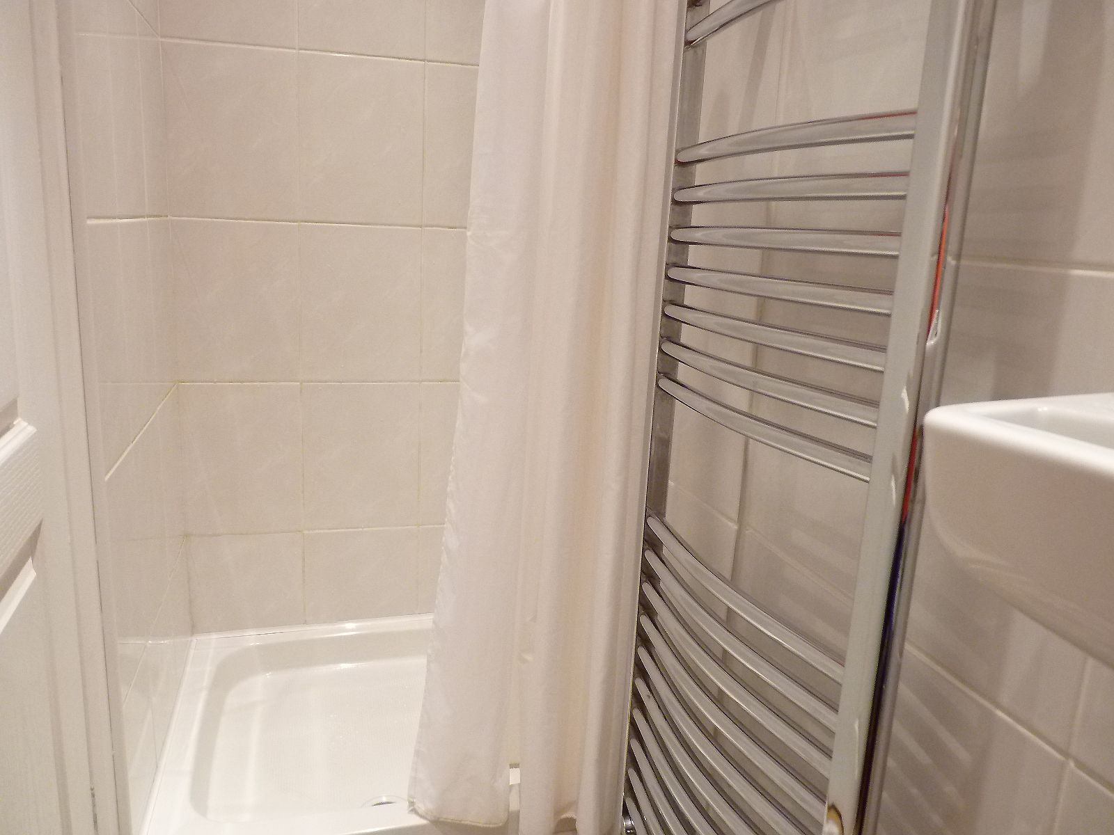 A shower area with a glass door, tiled walls, and a white shower curtain.