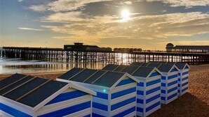Beach huts with sloped roofs, a pier extending into the water, and a sunset in the background. - Apollo Guest House (Hastings)