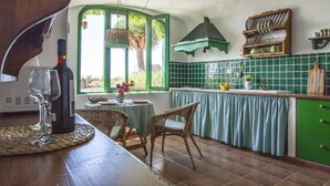 Una cocina con una mesa de comedor, sillas, una botella de vino y una ventana con vistas al verdor.