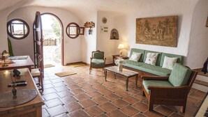 Una sala de estar acogedora con un sofá verde, una mesa de centro de madera y un sillón verde. Hay un cuadro en la pared y una puerta que da al exterior.