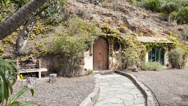 Un sendero de piedra que lleva a una casa rústica con una puerta de madera y un pequeño ventanal circular.