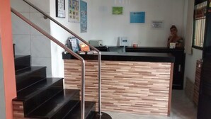 Un área de recepción con un mostrador de madera, una barra negra y una escalera con barandilla de metal.
