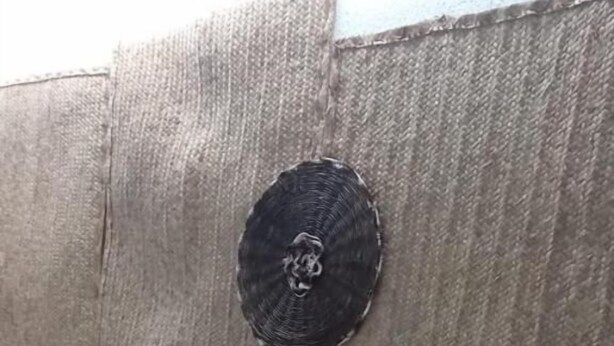Un espacio al aire libre con sillas de mimbre y una mesa redonda, una pared con un logotipo e información de contacto, y un suelo de baldosas.