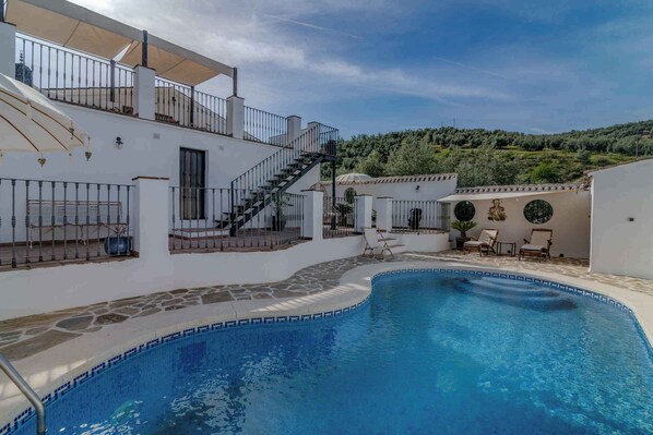 A pool area with a stone-tiled edge, a staircase leading to a covered balcony, and outdoor seating. - Romantic holiday home among the olive groves (Villanueva de Algaidas)