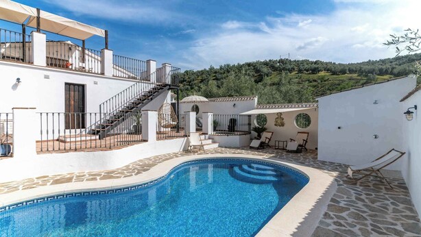 Una piscina con borde de piedra, una escalera que lleva a una terraza y vista de un paisaje montañoso.