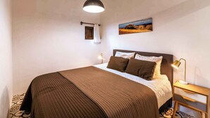 Una cama bien hecha con un edredón marrón, una lámpara de noche y un cuadro en la pared.