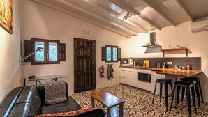 Un espacio habitable pequeño con sofá, una mesita, una zona de cocina con taburete y suelo de baldosas estampadas.
