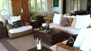A living room with wicker furniture, a wooden cabinet, and a glass candle on a side table. - Rockmere Villa - PANORAMIC OCEAN VIEWS, BEACH .2 MILES, MULTI-UNIT ESTATE (The Baths)