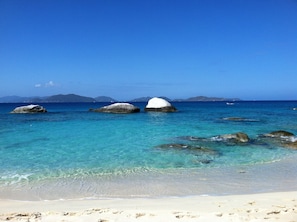 Una playa con agua turquesa cristalina, arena blanca y rocas grandes.