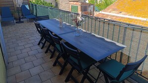 Une terrasse avec une table et des chaises, une bouteille et un vase rempli de fleurs.
