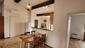 Une cuisine compacte avec un coin repas, comprenant une table et des chaises en bois, un luminaire suspendu et un petit réfrigérateur.