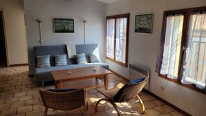 Une pièce chaleureuse avec un canapé, une table en bois, des chaises en osier et de grandes fenêtres avec des rideaux.