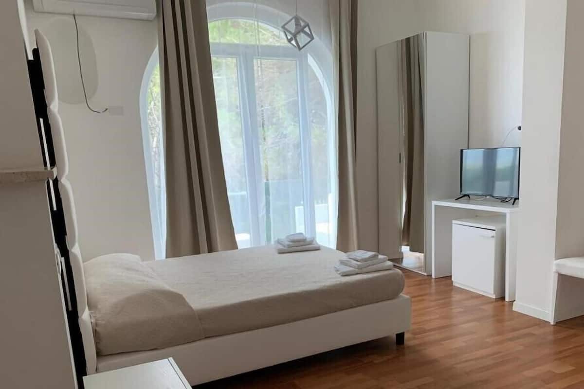 Una habitación de hotel moderna con una cama, un escritorio con televisor y vistas al exterior a través de amplios ventanales.