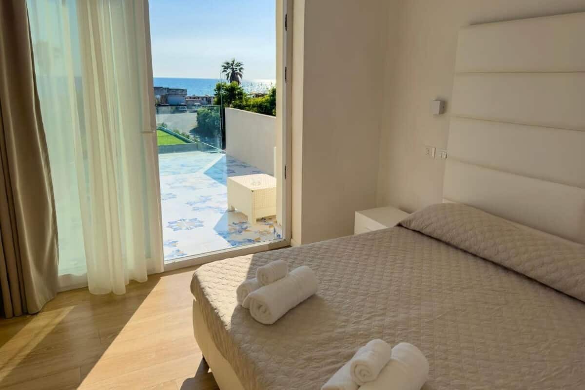 Un dormitorio con una cama grande, vista al mar y un balcón con una silla blanca.