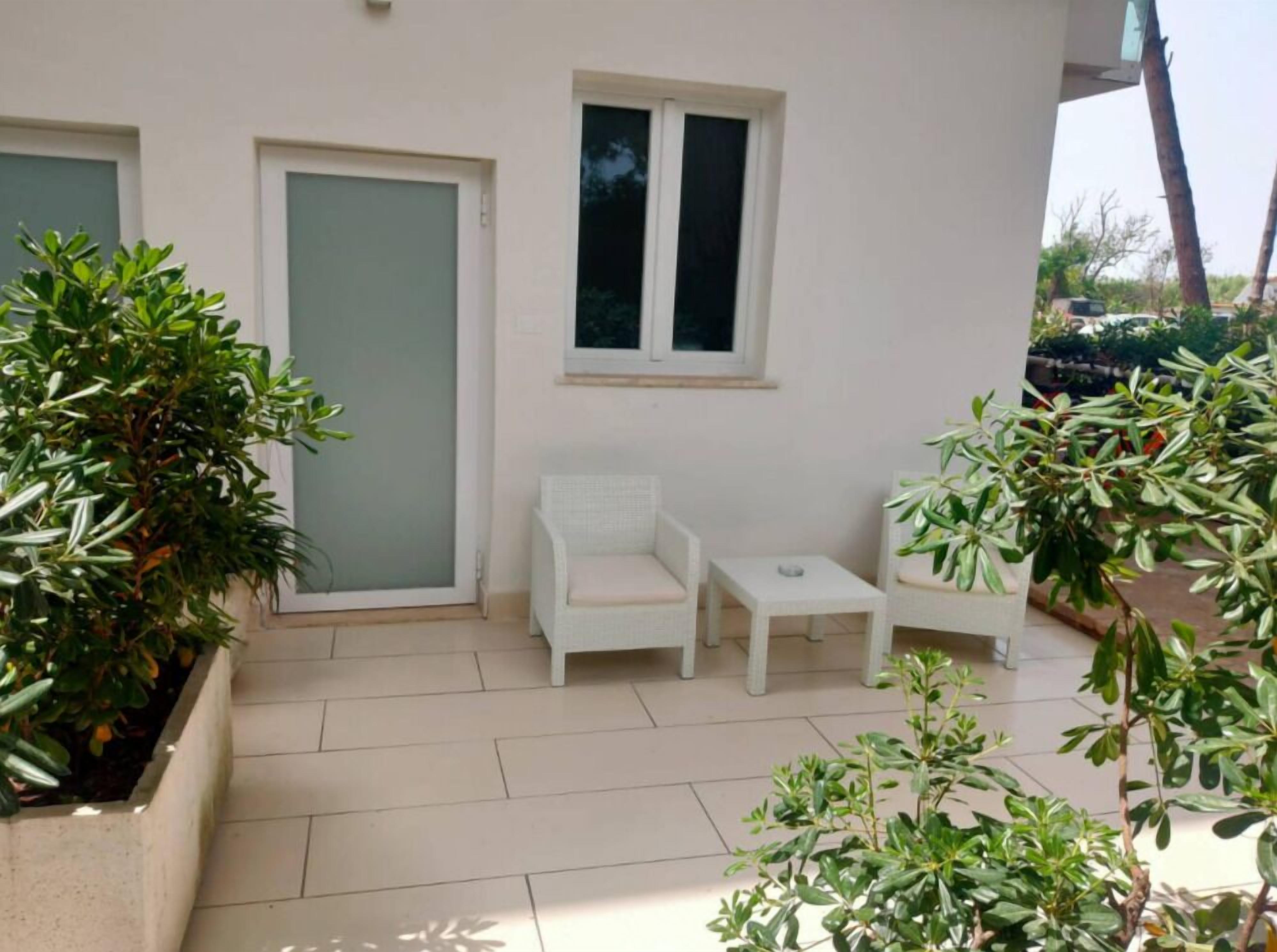 A small patio area with a white chair, a small table, and potted plants.