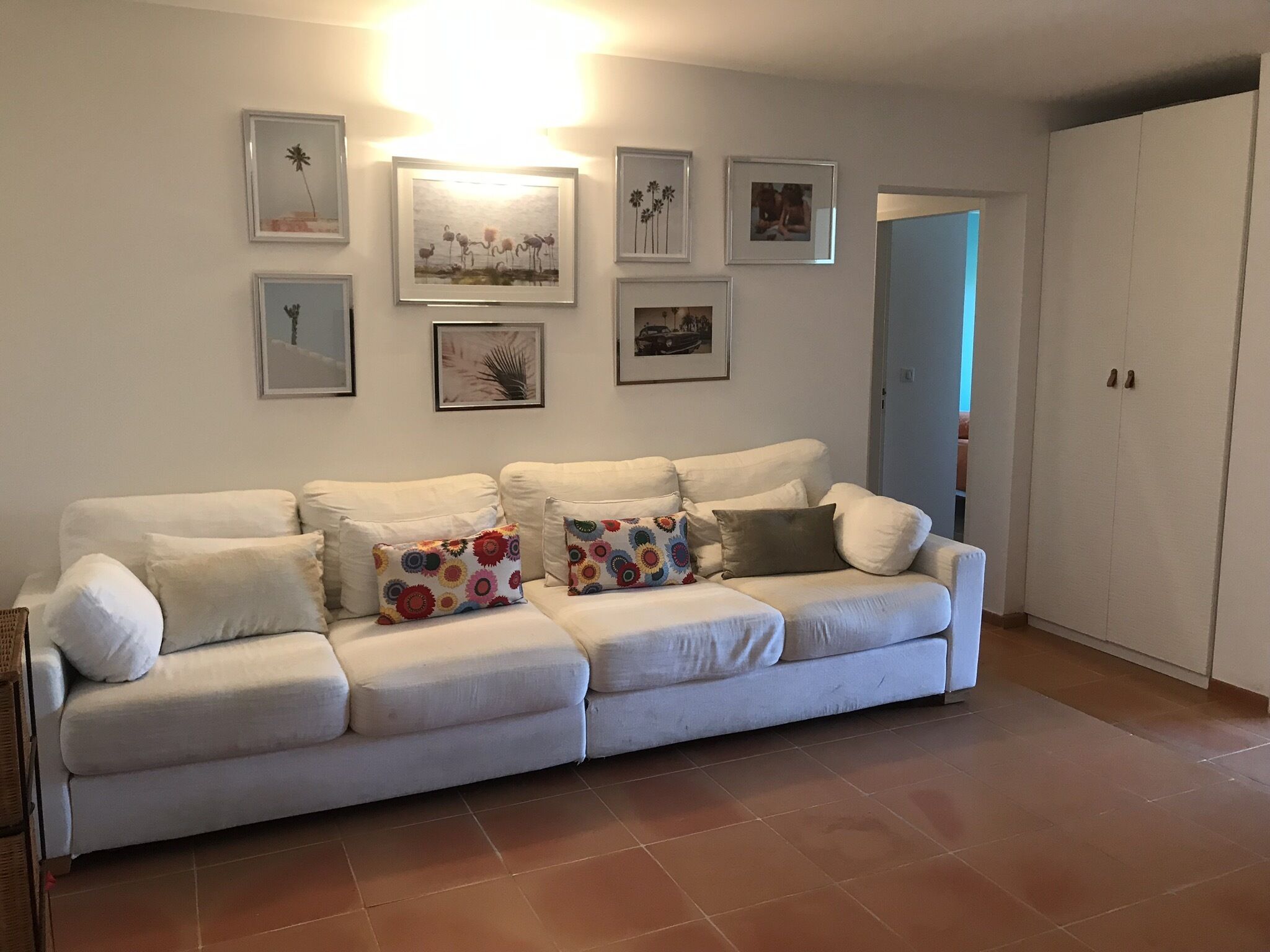 A white sofa with colorful pillows, a wall with framed pictures, and a wardrobe.