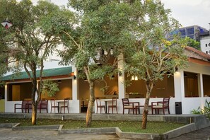 A building with outdoor seating and trees. - The Capsule Malioboro (Yogyakarta)