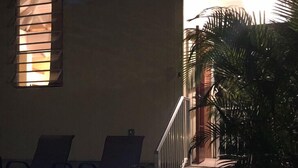 Een hottub met blauw licht, een raam met zonwering en een trap die leidt naar een balkon met palmbomen.