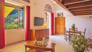 Une pièce chaleureuse avec un plafond en bois, une télévision, une table à manger avec des chaises, un buffet et une fenêtre ornée de rideaux rouges.