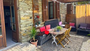 Un bâtiment en pierre avec une porte en bois, un patio doté d’un toit de chaume, une table avec des chaises et un canapé.