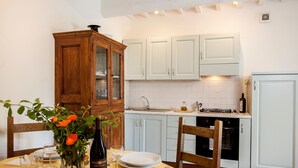 Un coin repas avec une table dressée pour deux personnes, un buffet en bois et, au fond, des meubles de cuisine aux couleurs claires.
