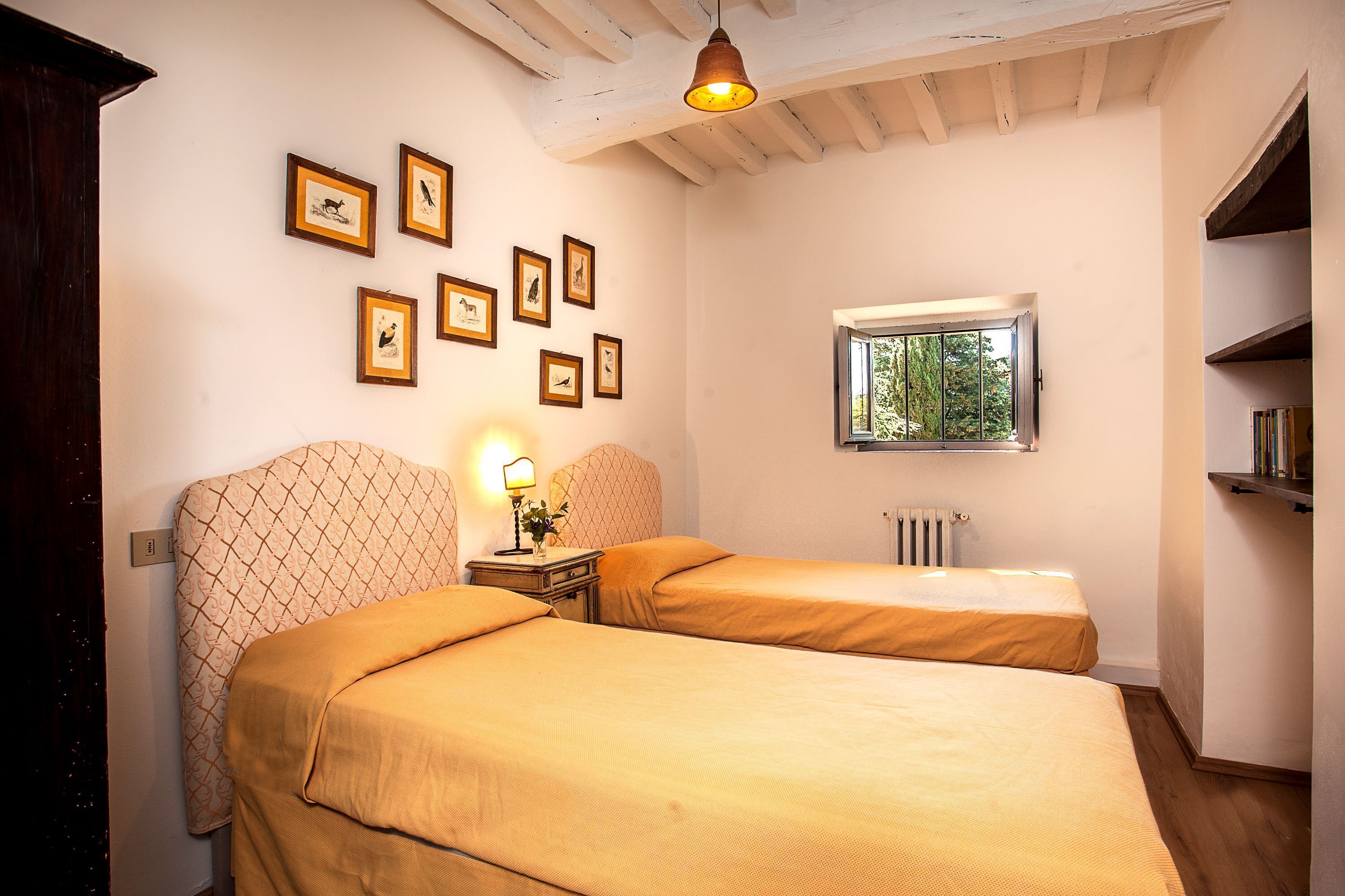 A room with two beds, a window with a view, and several framed pictures on the wall.