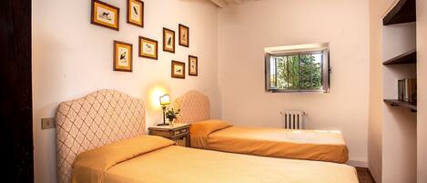 A room with two beds, a window with a view, and several framed pictures on the wall.