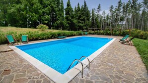 Une piscine rectangulaire bordée d’une terrasse en pierre, entourée d’une pelouse verdoyante et d’arbres.