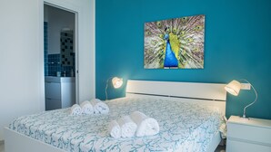 A bedroom with a bed, a headboard, a nightstand, a lamp, a wall-mounted painting, and a bathroom visible through an open door. - At the home of Giò, villa with pool (Marina di Ragusa)