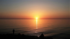 A sunset over a calm sea with a silhouette of a person fishing. - At the home of Giò, villa with pool (Marina di Ragusa)
