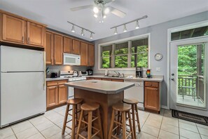 Una cocina moderna con armarios de madera, una isla central con taburetes, un refrigerador y una ventana con persianas.